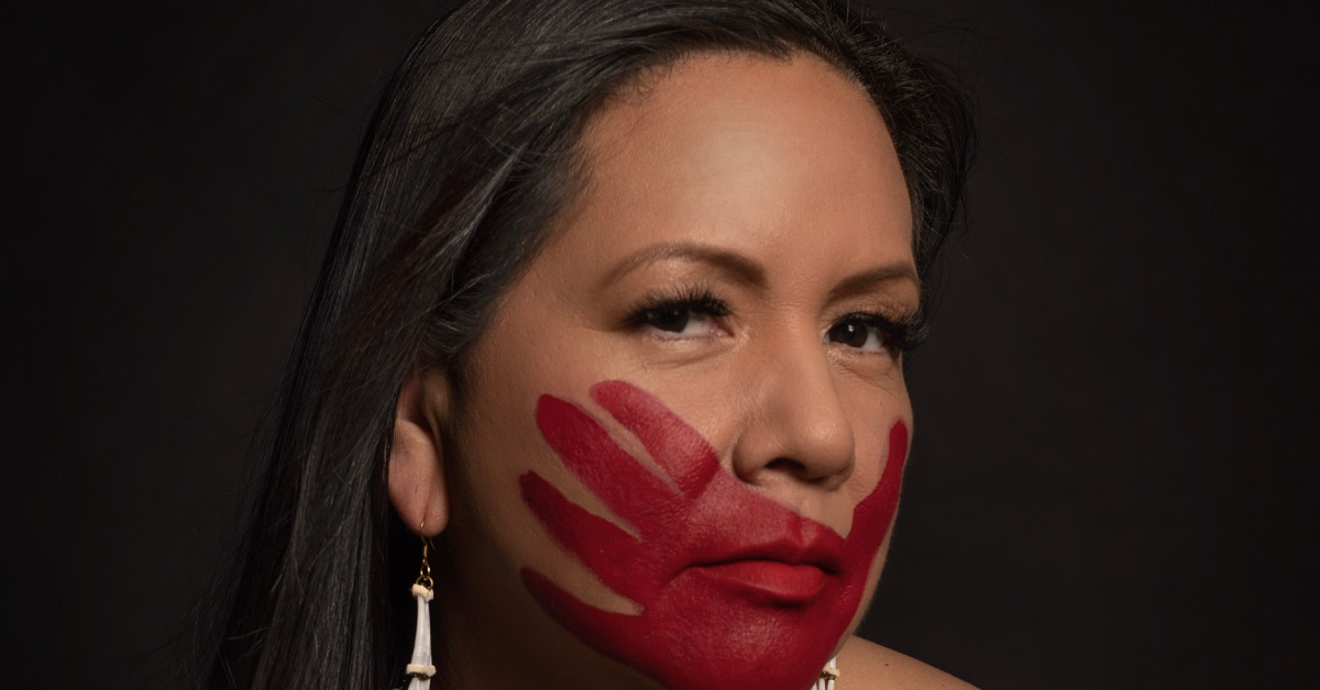 An Indigenous woman has a red handprint over her mouth for solidarity with the Missing and Murdered Indigenous Women movement.