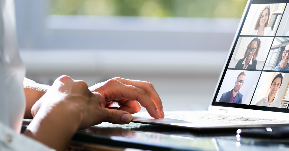 A close-up of a nondescript person sitting at their laptop with multiple people on the screen during a video call.