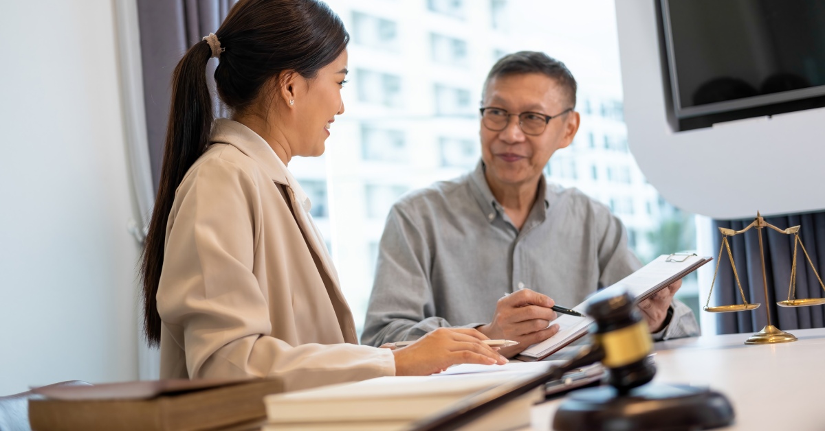 A client and her attorney sitting at a desk while the attorney points at a document on his clipboard.