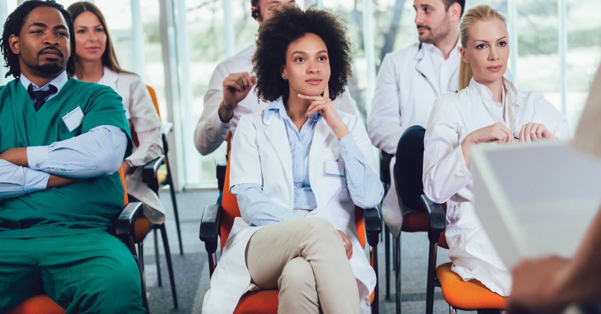 A group of doctors of varying races and genders sitting attentively in a conference room, listening to a seminar.