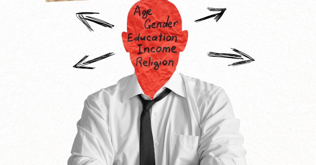 A man crossing his arms. He has a red paper head that reads "age, gender, education, income, religion" in black letters.