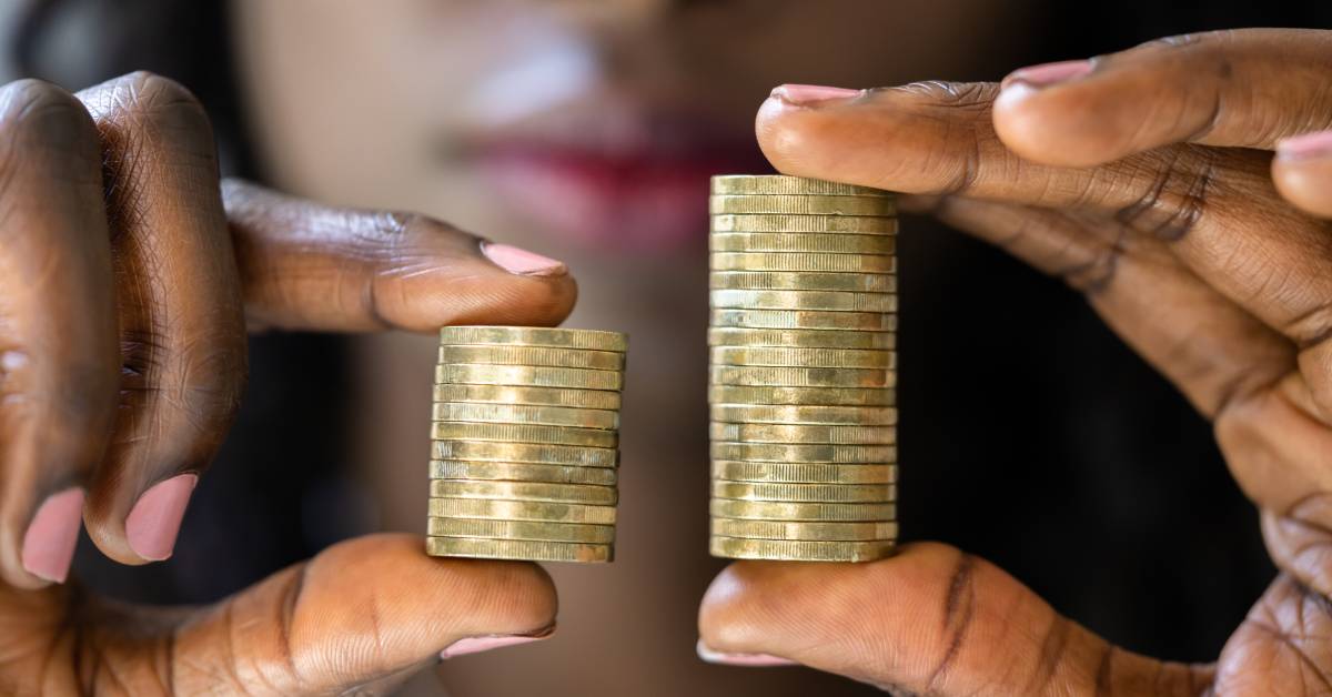 A close up of a woman of color holding two stacks of coins between her fingers; one is much shorter than the other.